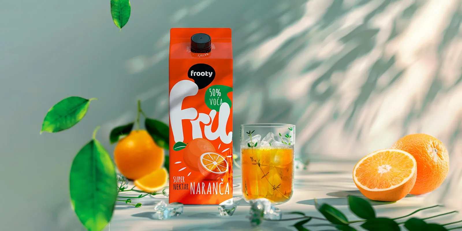 Frooty Fru orange nectar carton with 50% fruit beside iced glass and fresh oranges