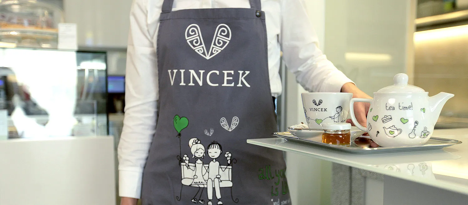 Vincek café server holding tea tray with branded teapot and cup