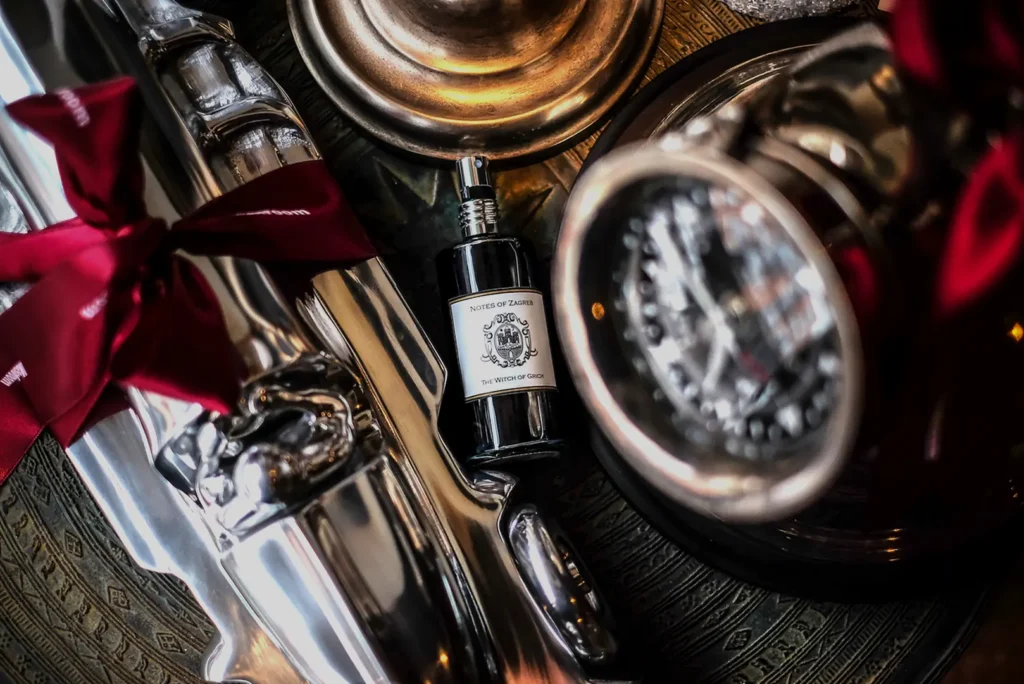 Notes of Zagreb "The Witch of Grich" perfume bottle among vintage brass objects and red ribbon